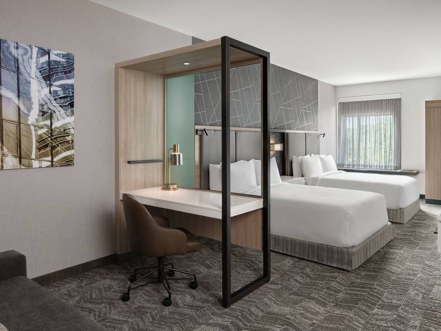 A hotel room with two beds, a desk, a chair, a TV, and a large window.