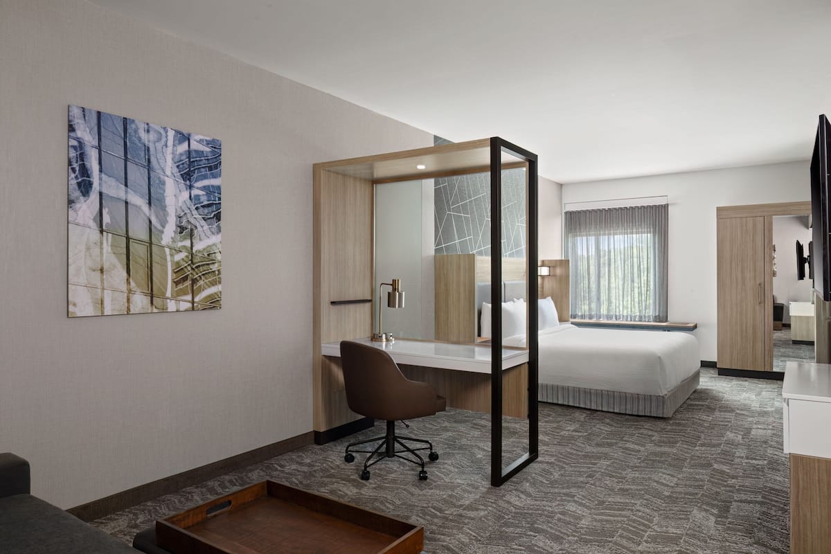 A hotel room with a bed, desk, chair, and a large mirror.