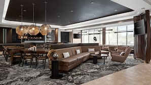 A modern living room with a brown sectional sofa, a dining area with wooden chairs, and a large window providing natural light. - Springhill Suites By Marriott Kalamazoo Portage (Portage)