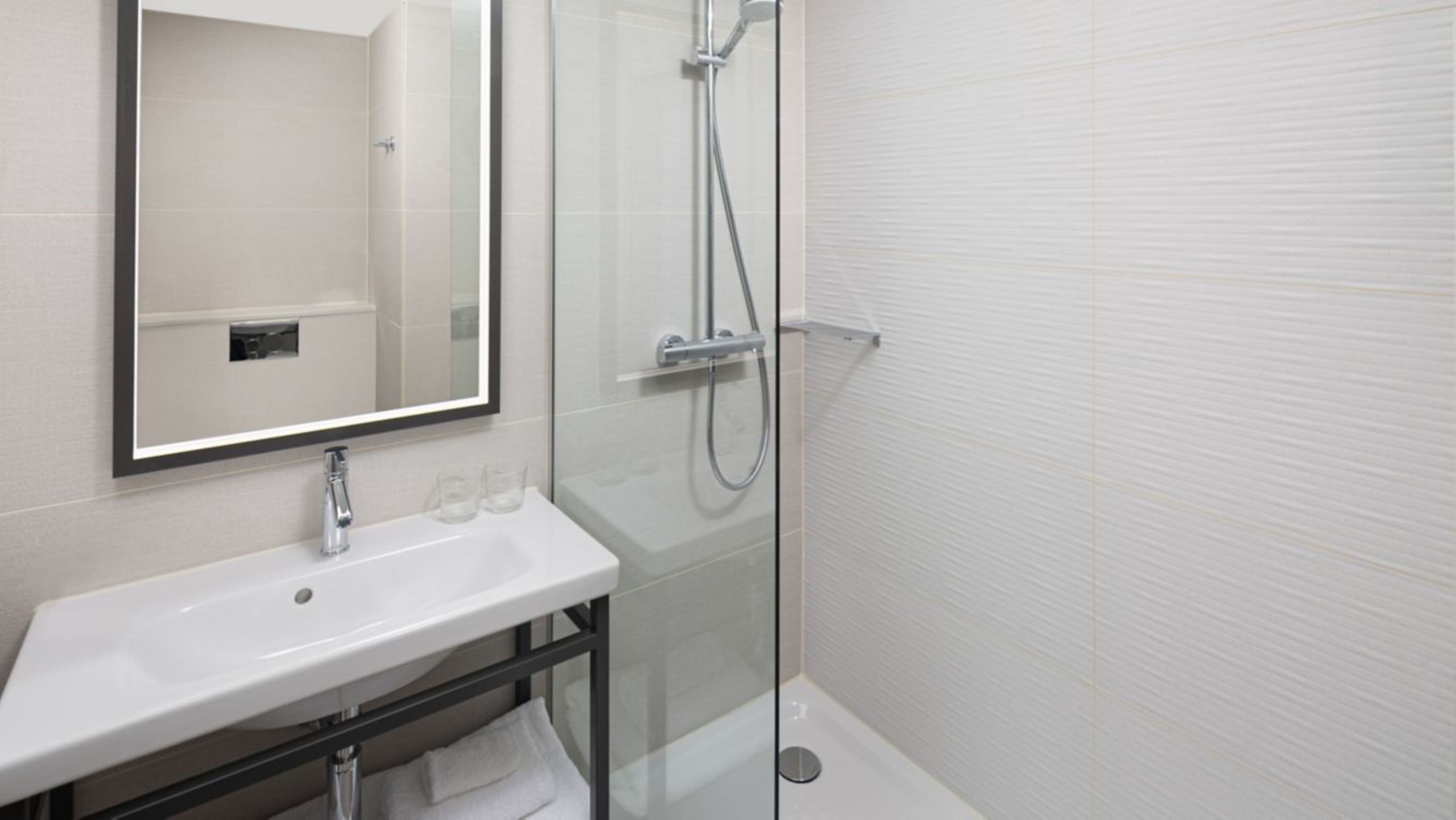 A modern bathroom with a white sink, a mirror, and a glass-enclosed shower.