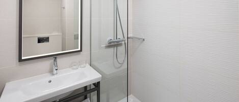 A modern bathroom with a white sink, a mirror, and a glass-enclosed shower.