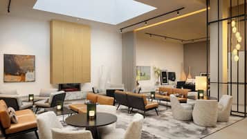Eine moderne Hotelhalle mit hoher Decke, Oberlichtern und verschiedenen Sitzbereichen, darunter Sofas und Sessel.
