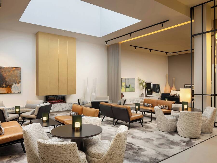 Eine moderne Hotelhalle mit hoher Decke, Oberlichtern und verschiedenen Sitzbereichen, darunter Sofas und Sessel.