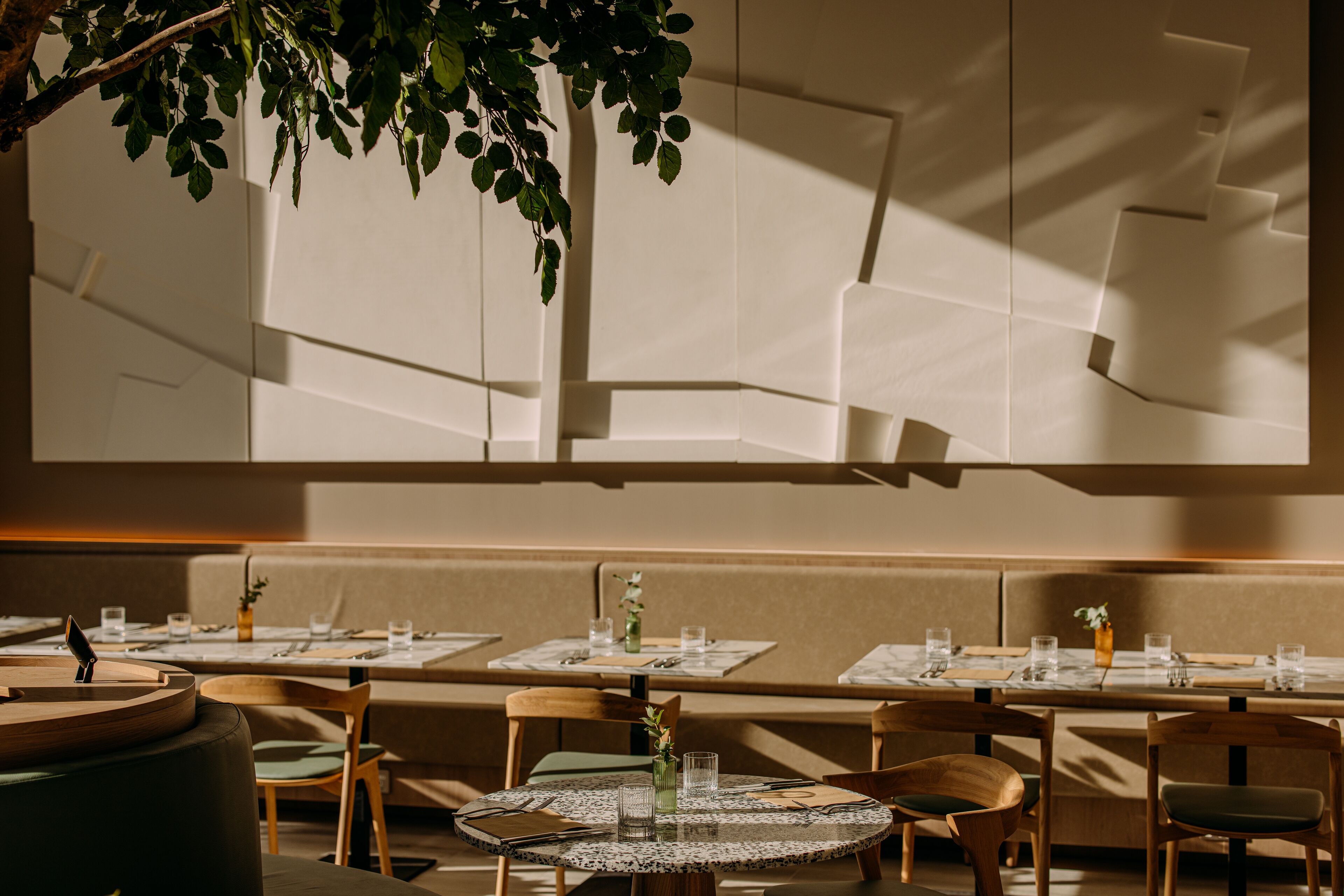 A restaurant with round tables, wooden chairs, and a large window with geometric patterns.