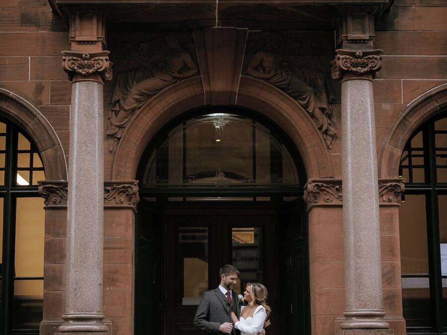 Una pareja de pie frente a un edificio con un gran arco y elaborada ornamentación de piedra.