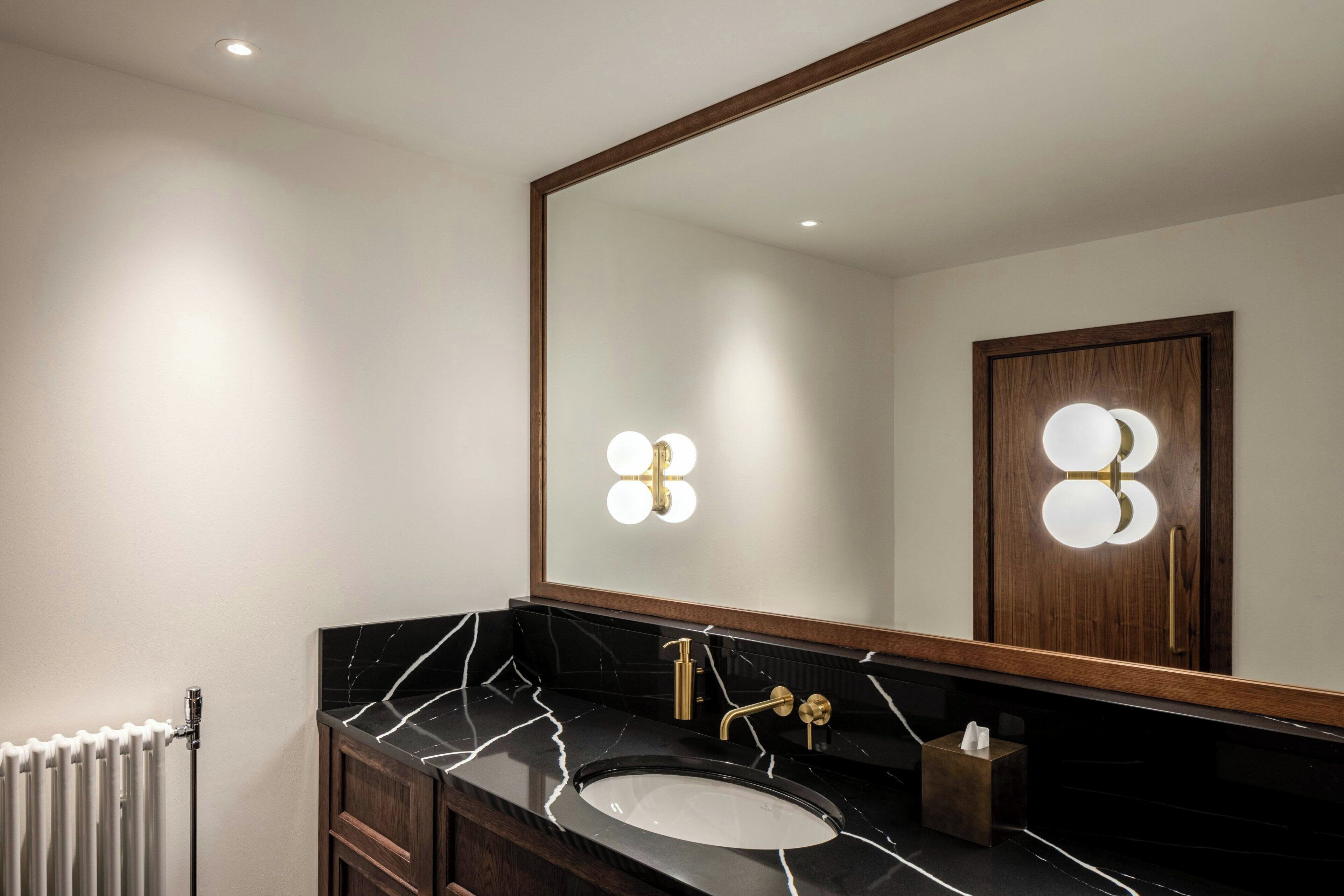 Ein Badezimmer mit einem schwarzen Marmorbecken, goldenen Armaturen und Wandleuchten.