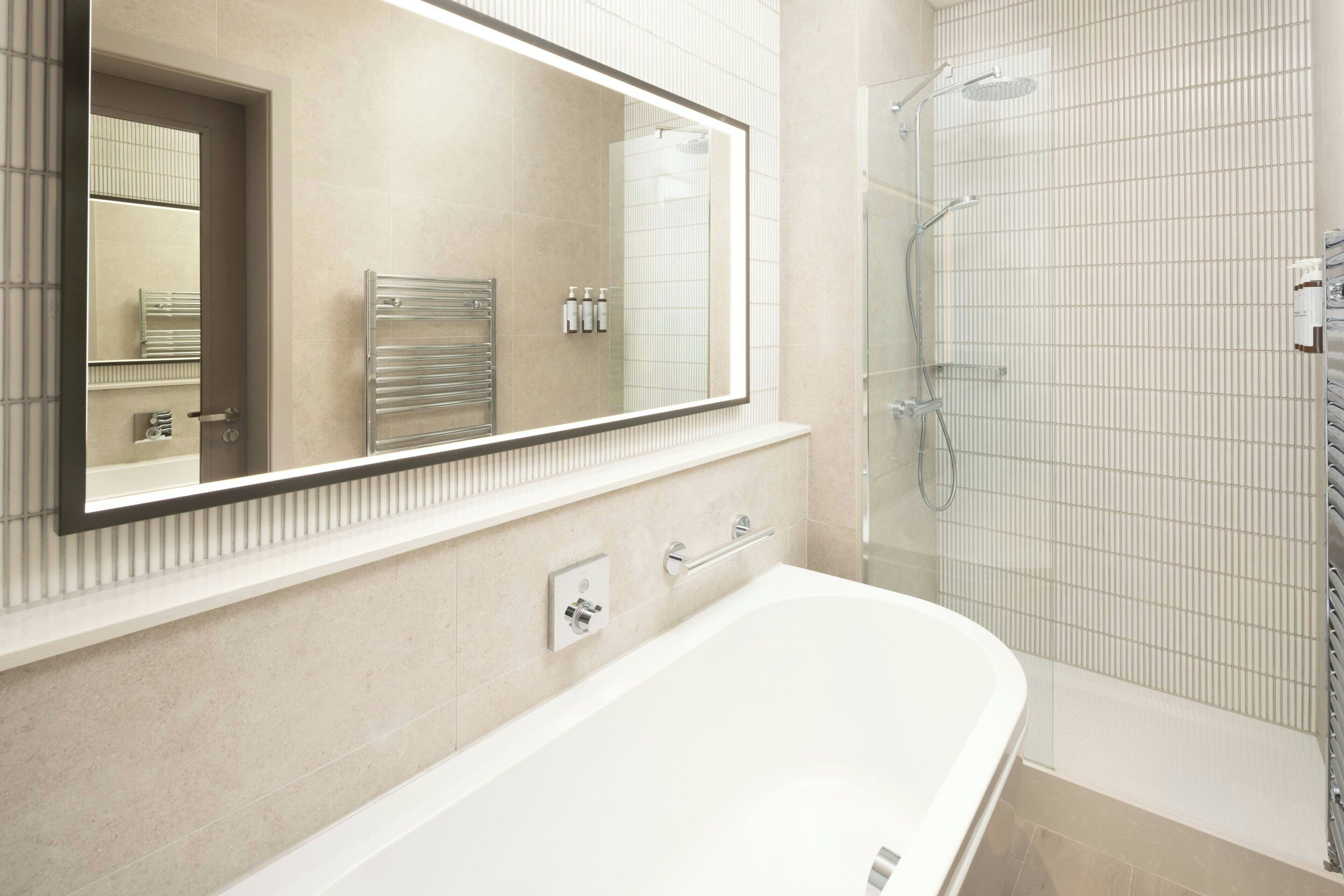 Un baño moderno con un espejo grande, una bañera, una ducha y un perchero para toallas.