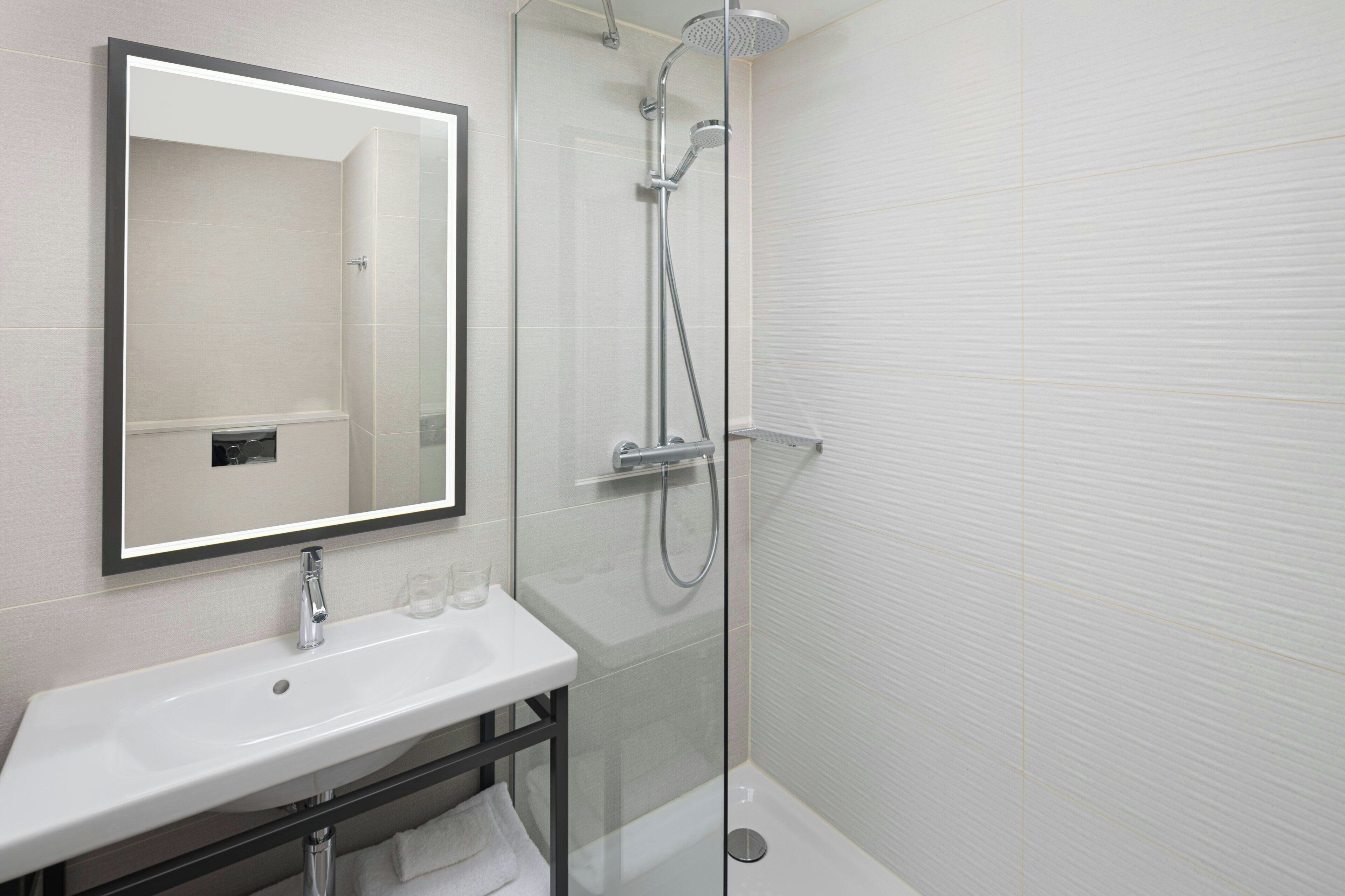 Une salle de bain moderne avec une douche à parois de verre, un lavabo blanc et un grand miroir.