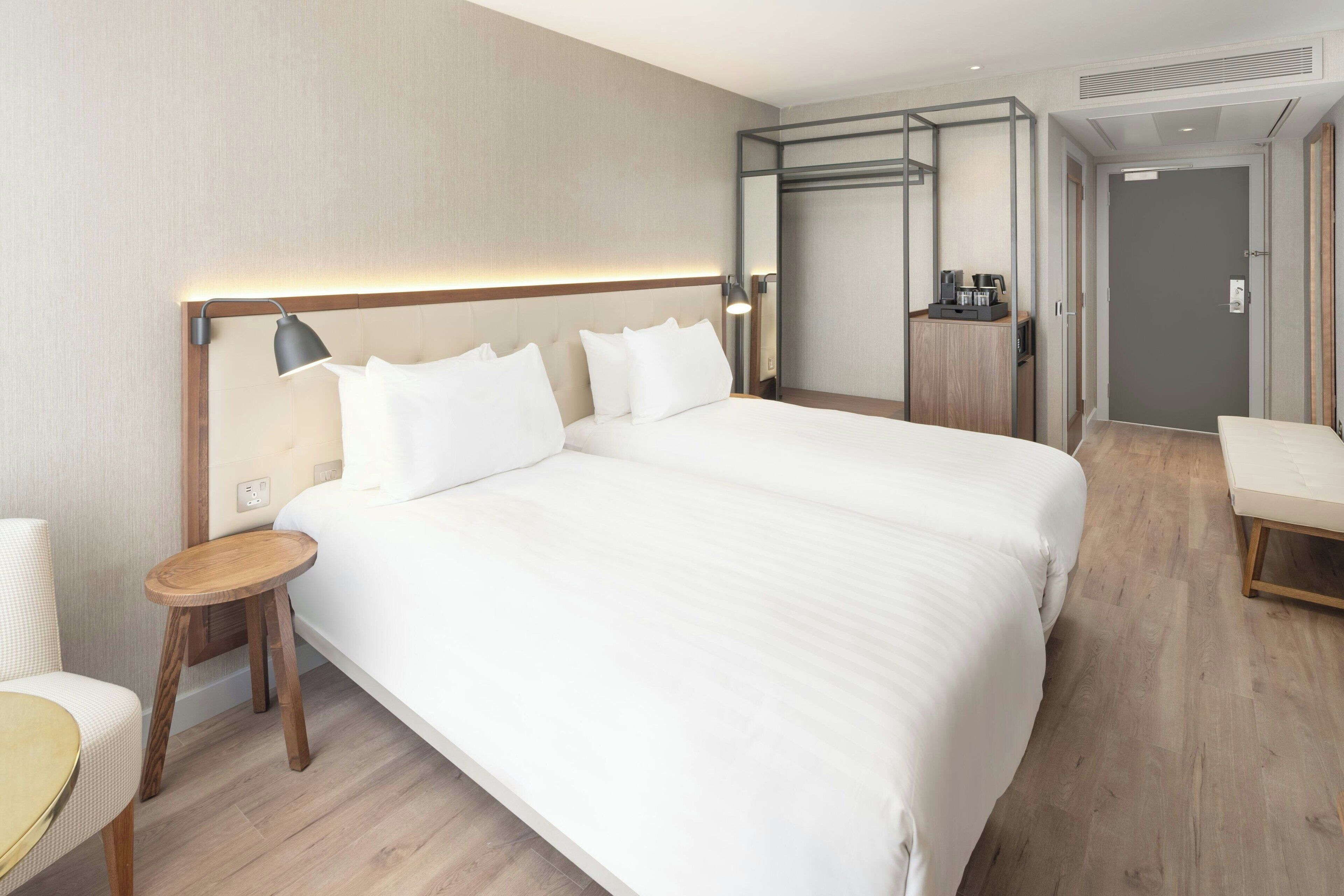 Una habitación de hotel moderna con una cama grande, una mesita de noche, una silla, un armario y una pequeña cocina.
