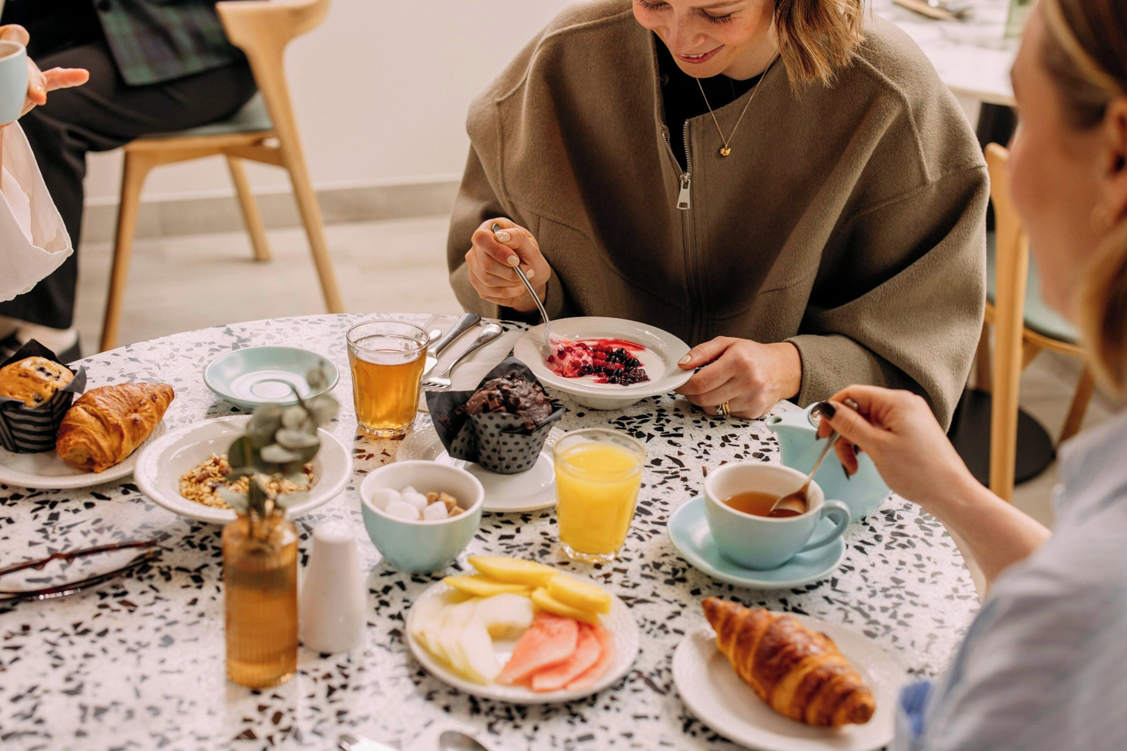 Un desayuno con croissants, fruta y bebidas sobre una mesa moteada.