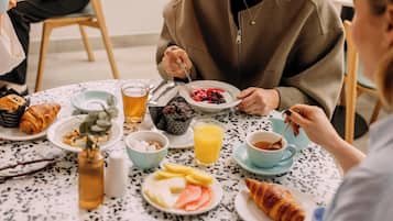Un desayuno con croissants, fruta y bebidas sobre una mesa moteada.
