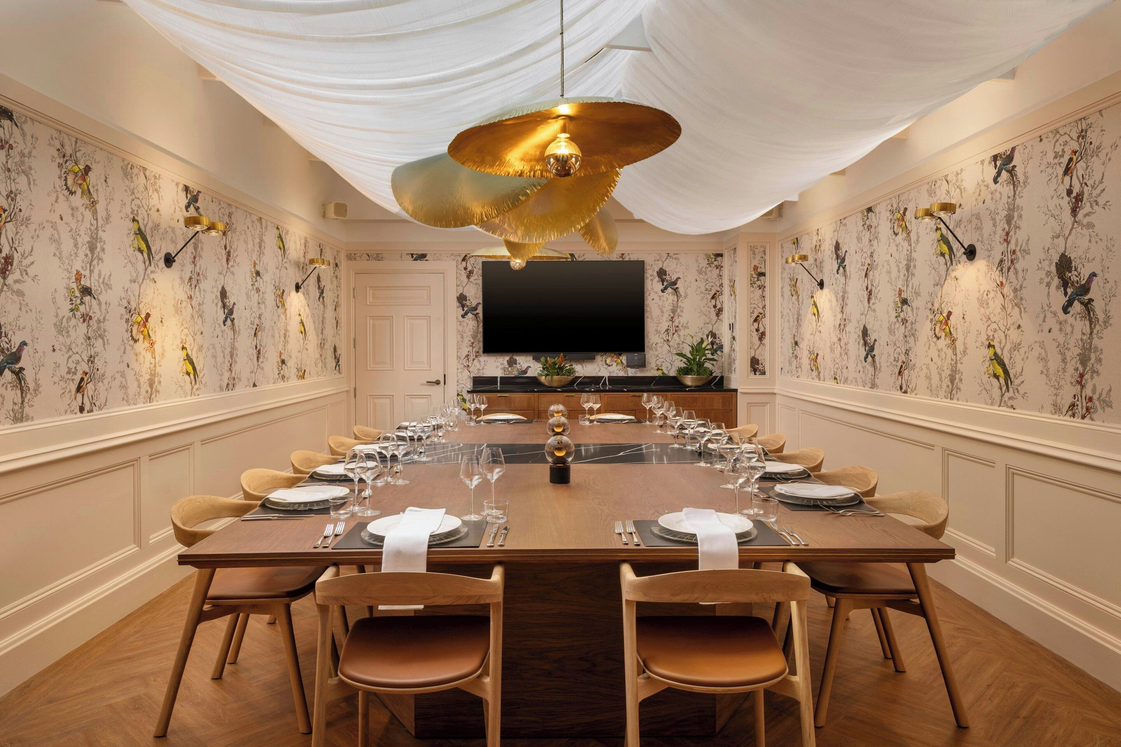 A formal dining room with a long wooden table set for a meal, flanked by chairs, and a large chandelier above.