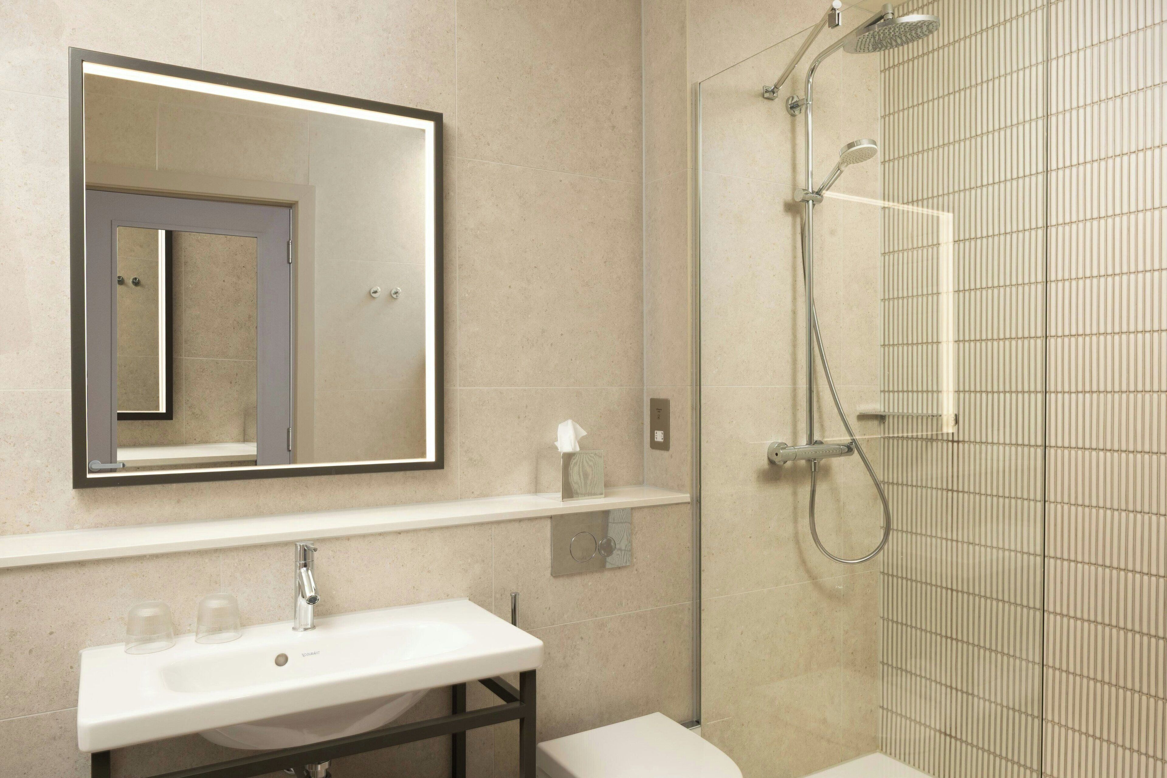 Een moderne badkamer met een grote spiegel, een witte wastafel, een toilet en een douche met glazen wanden.