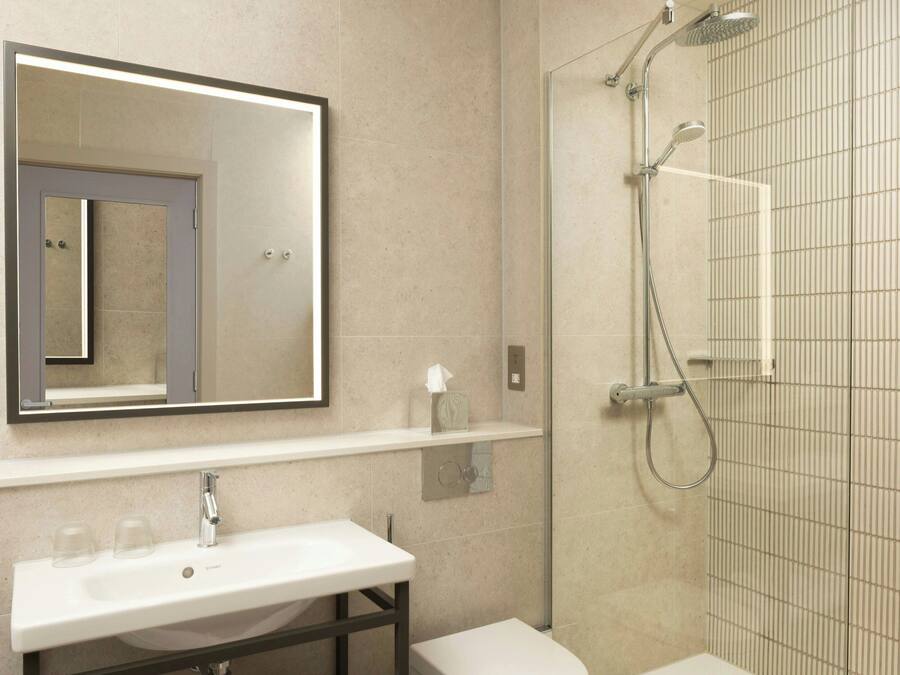 Een moderne badkamer met een grote spiegel, een witte wastafel, een toilet en een douche met glazen wanden.