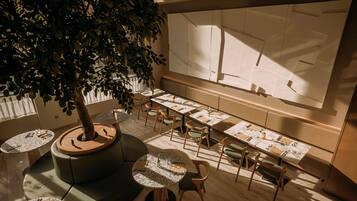 A modern dining area with round tables, green chairs, and a central tree.