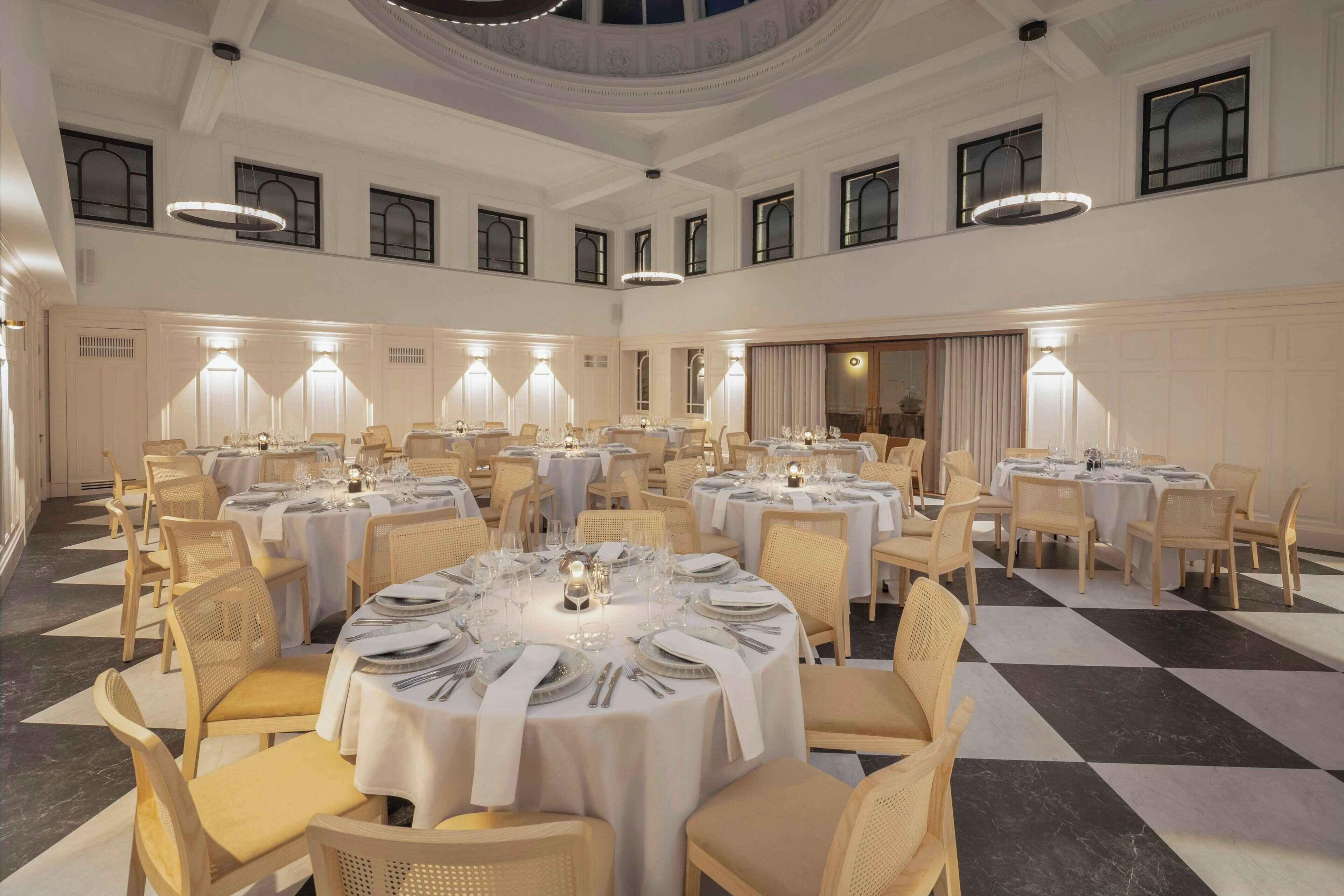 Un amplio salón de banquetes con varias mesas redondas dispuestas para comer, con manteles blancos y centros de mesa con velas.