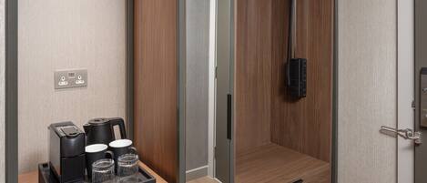 Une chambre d’hôtel avec une armoire en bois, une petite table avec une machine à café et des verres, et un espace douche.