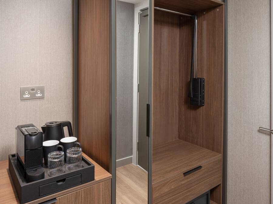 A hotel room with a wooden wardrobe, a small table with a coffee maker and glasses, and a shower area.