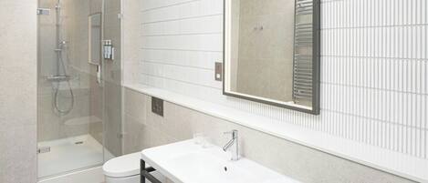 Un baño moderno con cabina de ducha de vidrio, un lavabo blanco con espejo arriba y un inodoro.