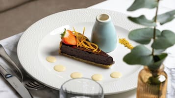A dessert plate with a chocolate tart, a strawberry, and a small blue cup, accompanied by a glass of water and a vase with a plant.