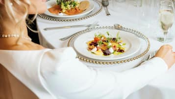 Una mesa de comedor con platos de comida, cubiertos y una copa de vino blanco.