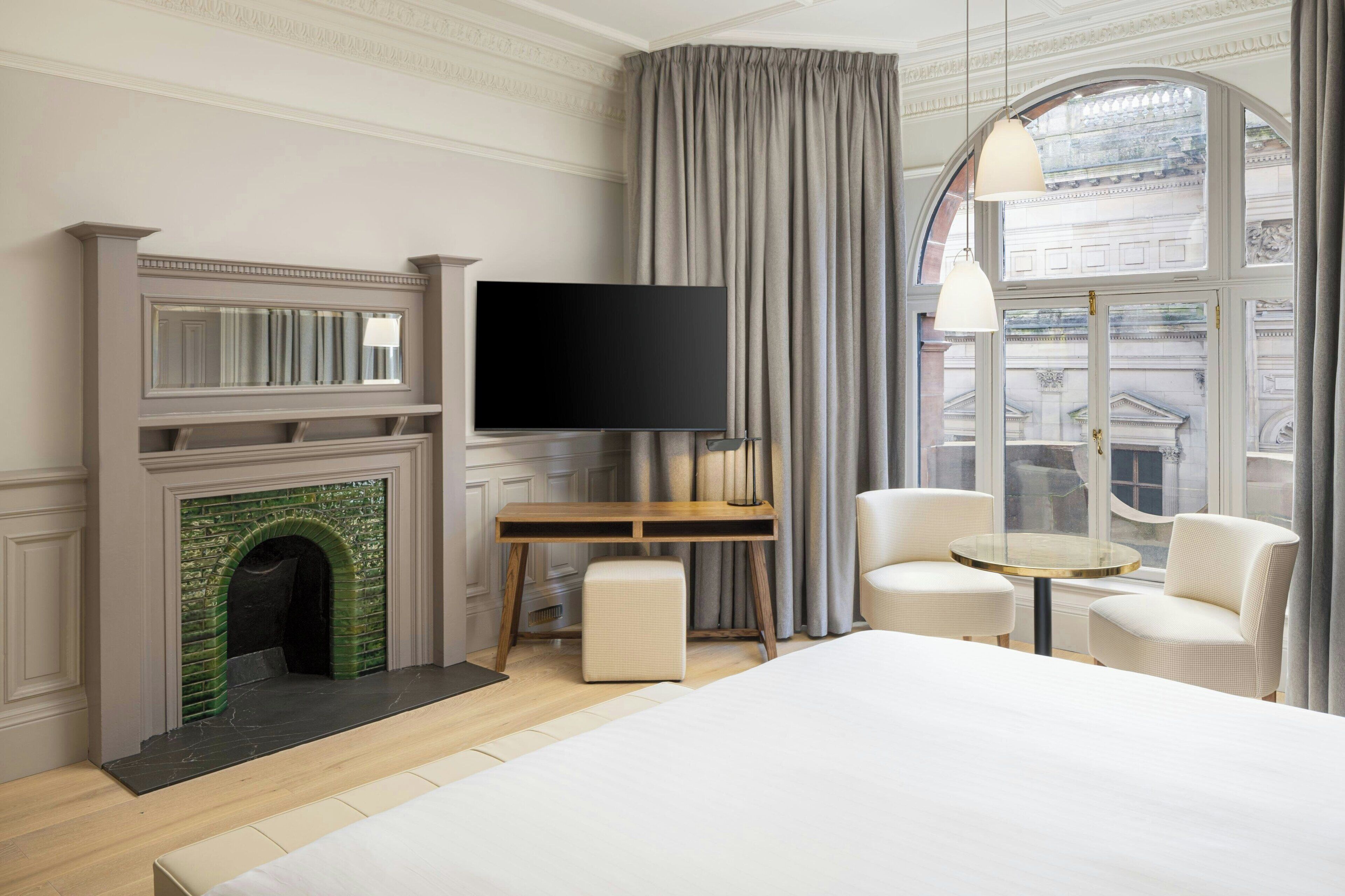 Una habitación de hotel moderna con chimenea, televisor de pantalla plana, escritorio, dos sillas y una cama grande.