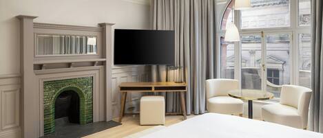 Una habitación de hotel moderna con chimenea, televisor de pantalla plana, escritorio, dos sillas y una cama grande.
