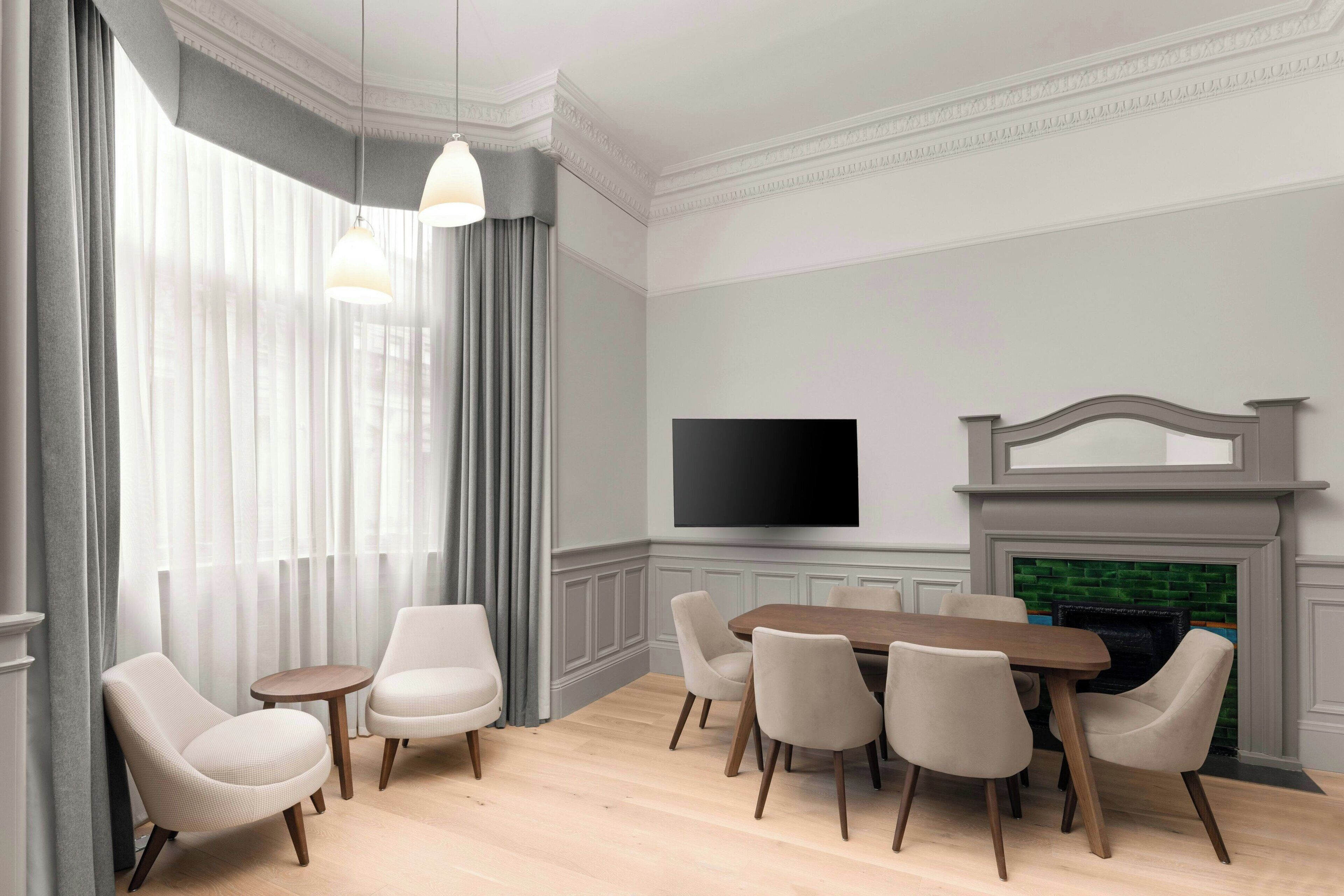 A dining room with a wooden table and six chairs, a flat-screen TV on the wall, and a fireplace.