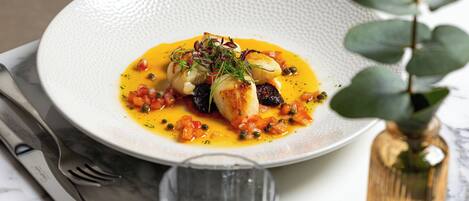 A white textured plate with a seafood dish, a glass of water, and a small vase with a plant on a marble table.