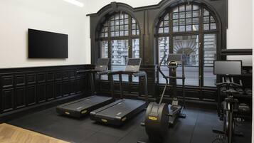 A gym with treadmills, a stationary bike, and a rowing machine, with large windows and a black and white color scheme.