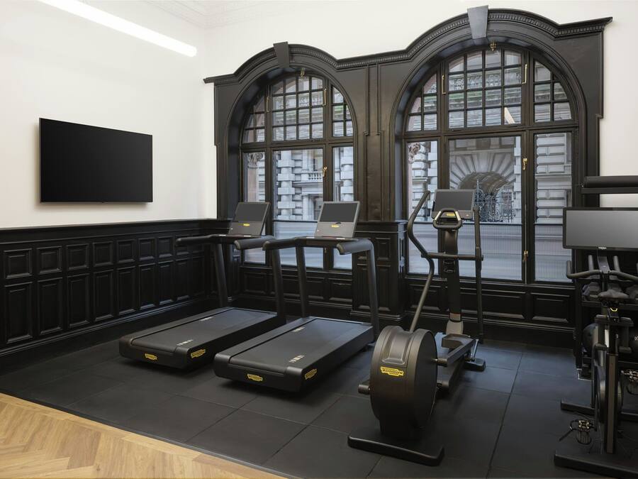 A gym with treadmills, a stationary bike, and a rowing machine, with large windows and a black and white color scheme.