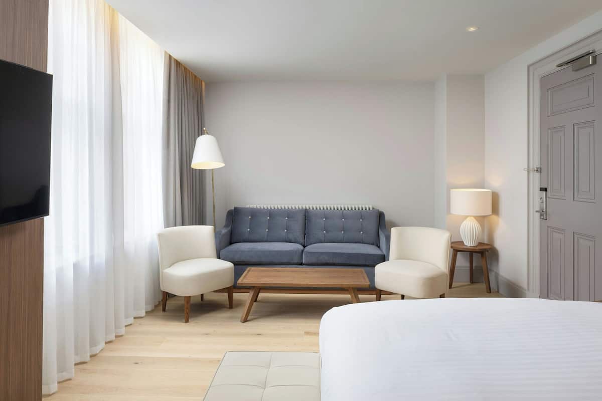 Ein modernes Hotelzimmer mit einem großen Bett, einer Couch, zwei Sesseln, einem Holztisch, einem Flachbildfernseher und einer Lampe.