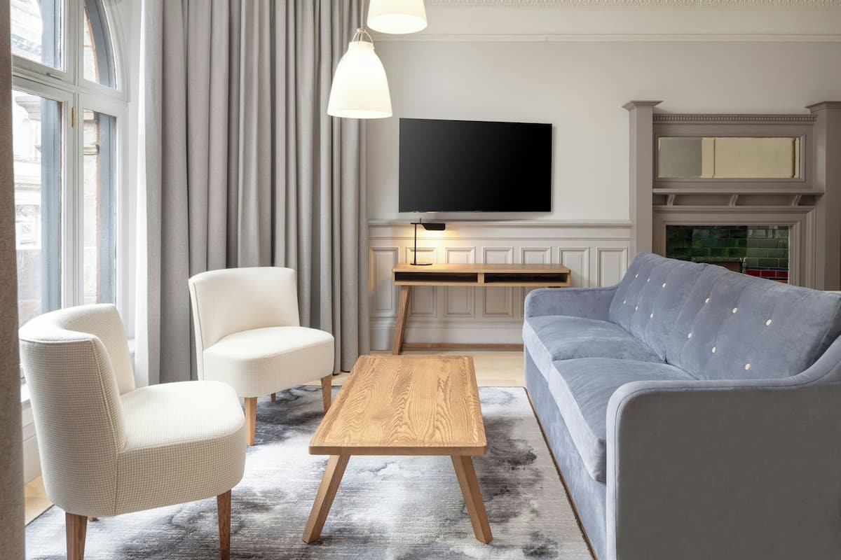 Ein modernes Wohnzimmer mit einem grauen Sofa, weißen Sesseln, einem Holztisch und einem flachbildfernseher an der Wand.