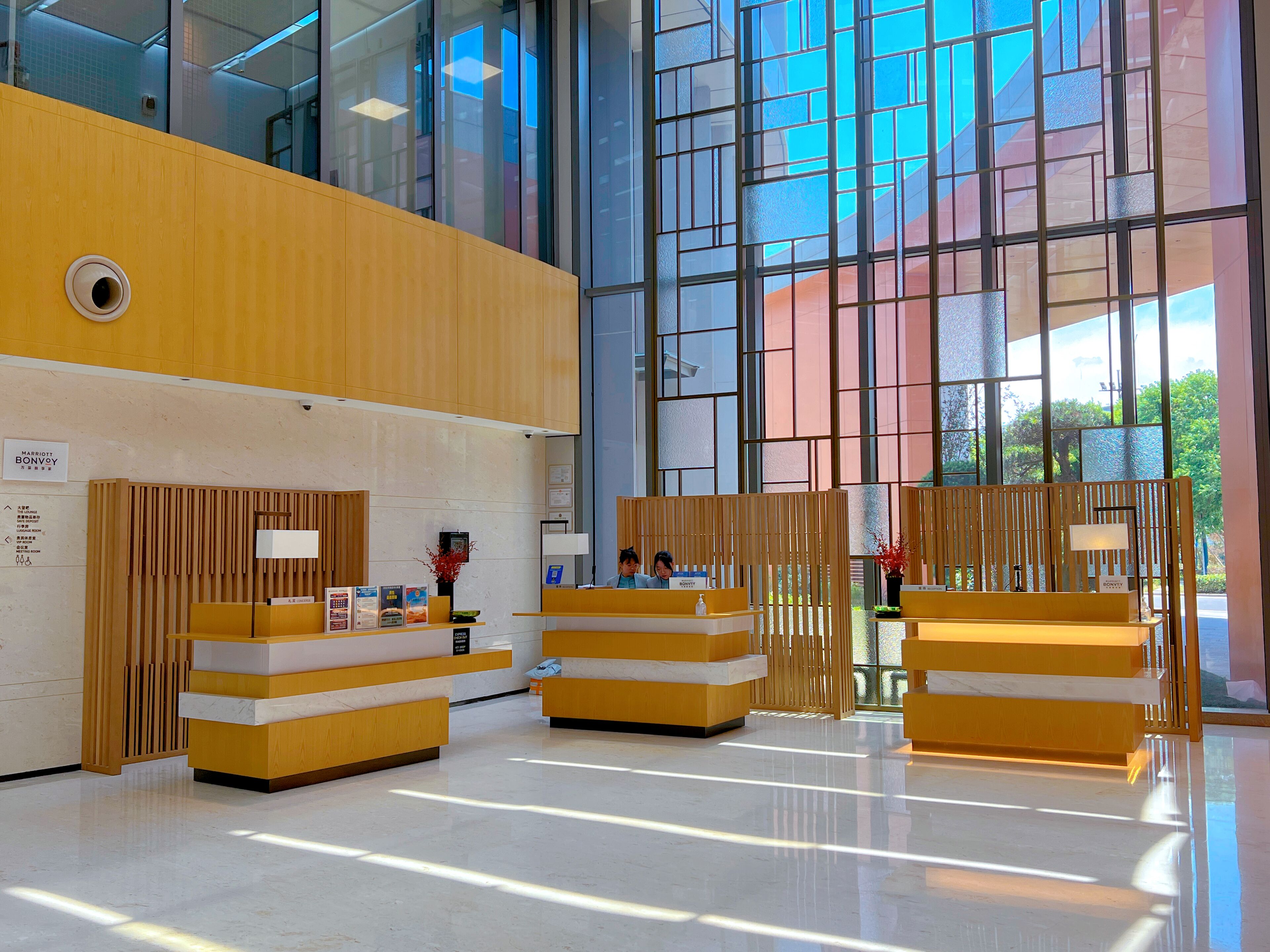 Zona d'entrada d'un hotel modern, amb taulells de recepció de fusta, un gran finestral i un rètol amb el nom de l'hotel.