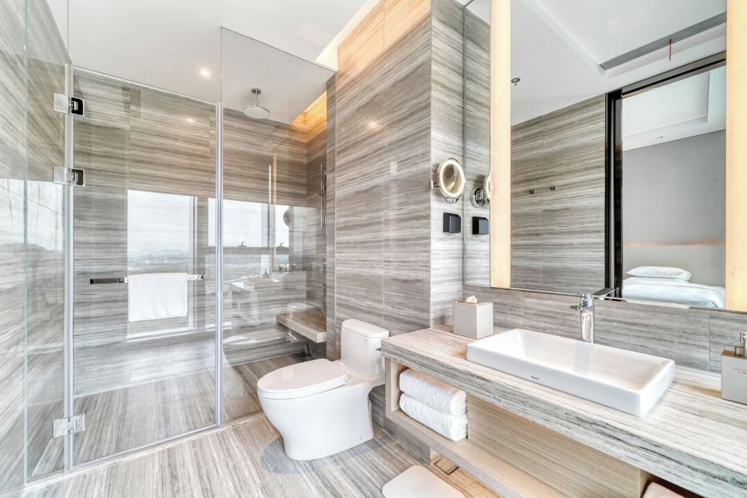 Un baño moderno con cabina de ducha de vidrio, inodoro blanco, lavamanos grande y espejo.