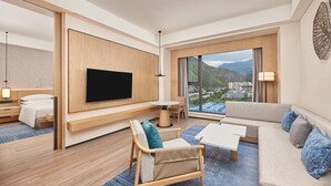 Une chambre d’hôtel moderne dotée d’une grande télévision, de sièges confortables, d’un coin repas et offrant une vue sur la ville.