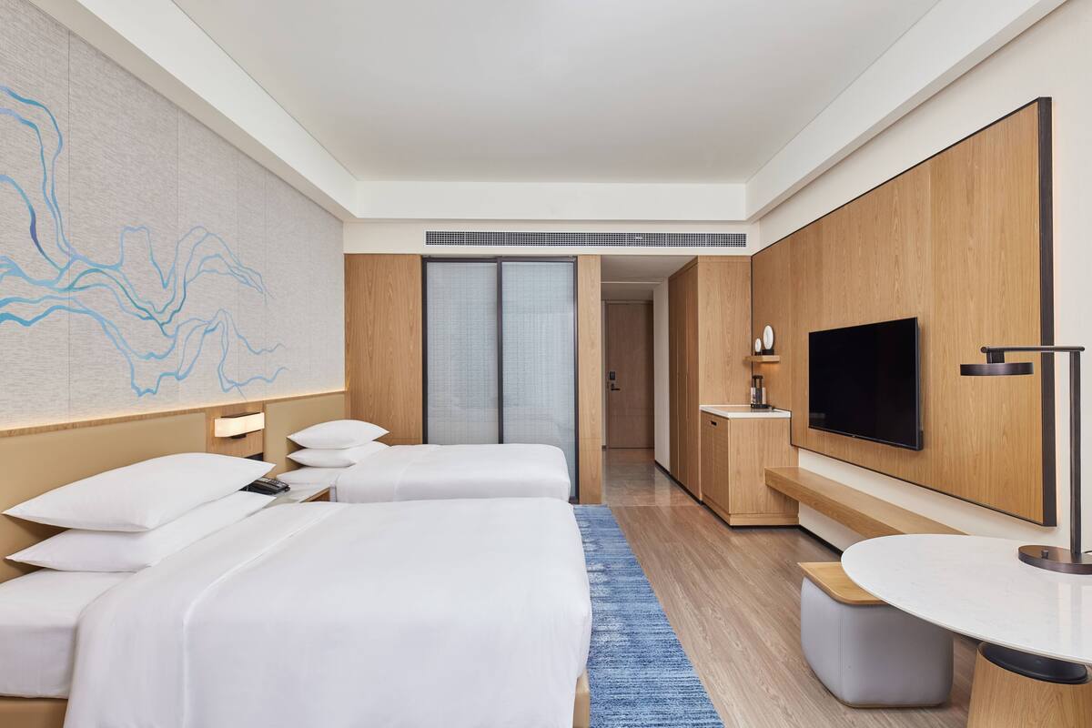 Habitación de hotel con dos camas, televisión, escritorio y baño.