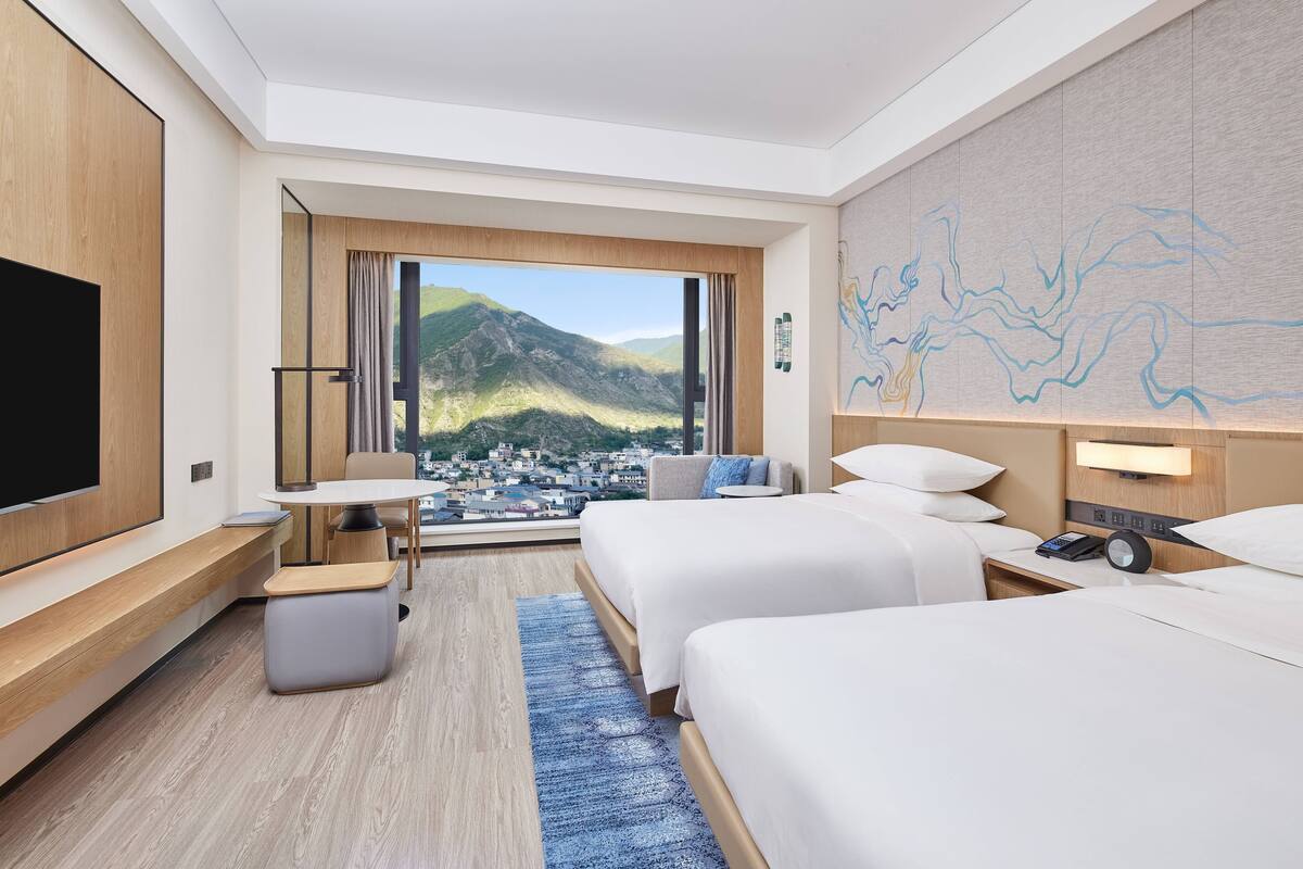 Habitación de hotel con dos camas, televisión, escritorio y vista a las montañas.