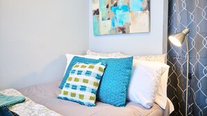 A bed with a patterned pillow, a blanket, and a wall-mounted abstract painting.
