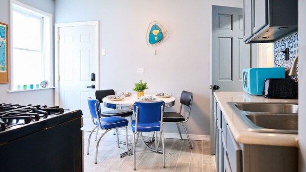A kitchen with a gas stove, a sink, and a dining area with blue chairs and a round table.