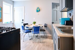 A kitchen with a gas stove, a sink, and a dining area with blue chairs and a round table.
