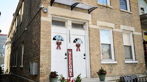 A brick building with a white double door, number 1503, and a 'WELCOME' sign. There are Christmas decorations and potted plants in front.