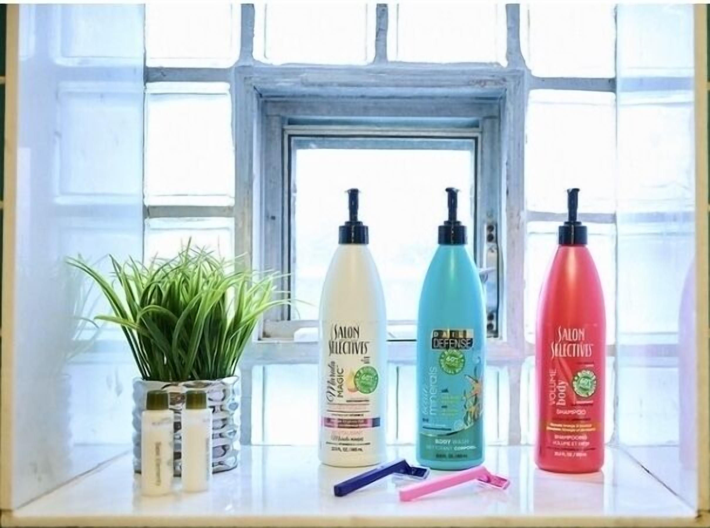 Une étagère avec quatre flacons de produits de soins pour le corps de la gamme Salon Selectives, une petite plante en pot et une paire de ciseaux.