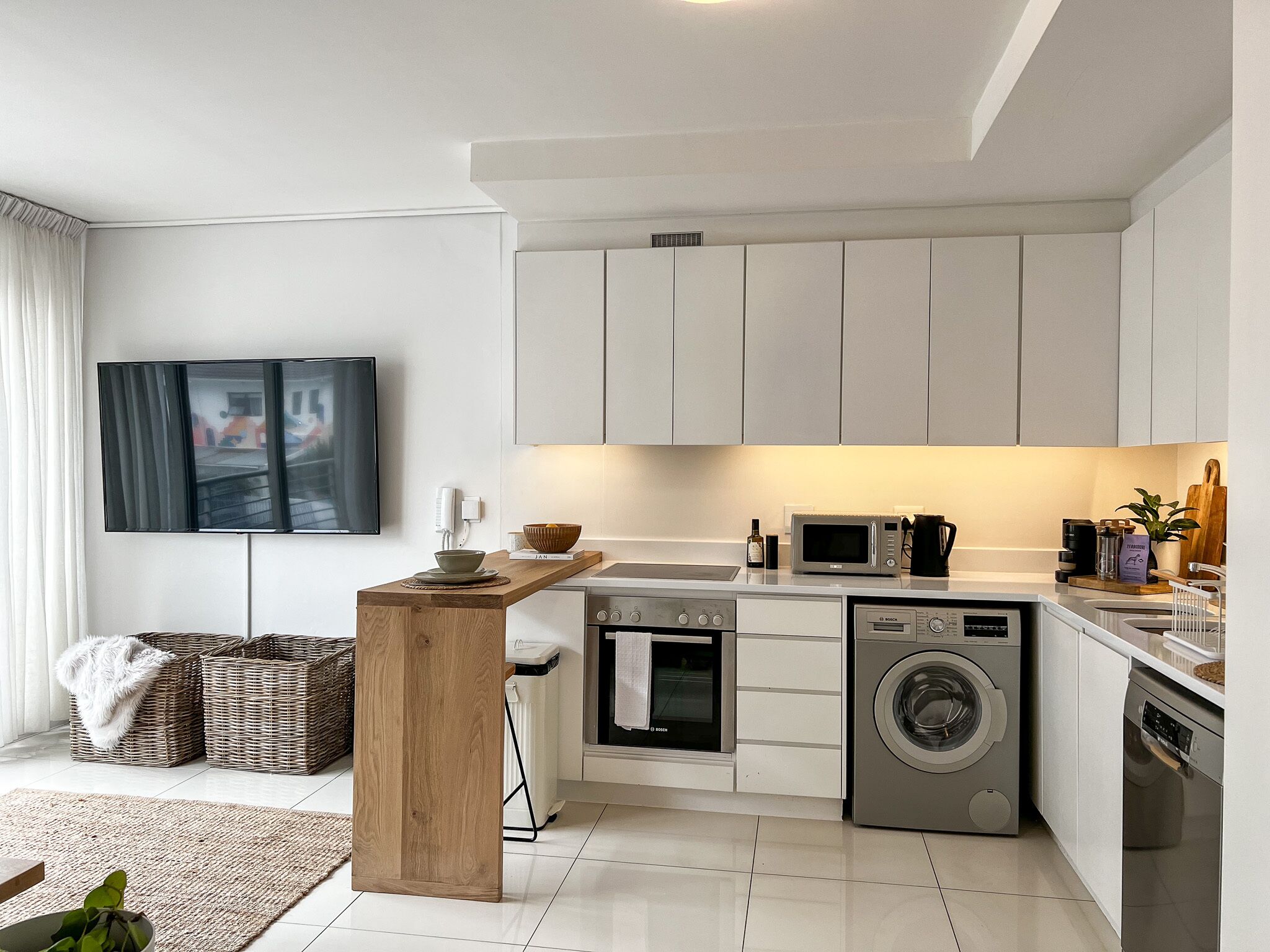 Eine moderne Küche mit weißen Schränken, einer Holz-Kochinsel, einem eingebauten Backofen, einer Waschmaschine und einer Mikrowelle.