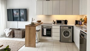 Une cuisine moderne avec des meubles blancs, un îlot central en bois, un four encastré, un lave-linge et un four à micro-ondes.