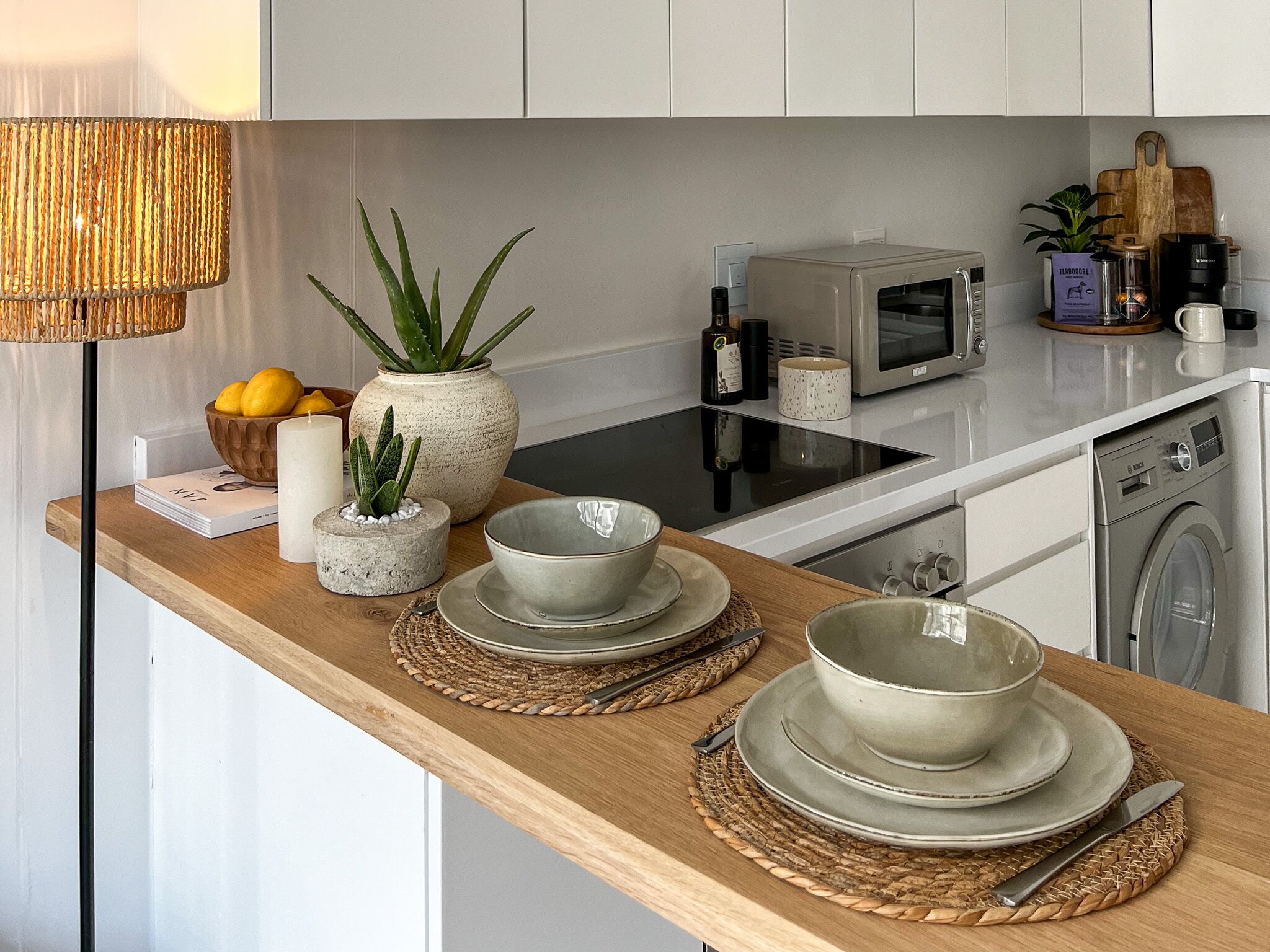 A modern kitchen with a wooden countertop, a microwave, a washing machine, and various kitchen items.