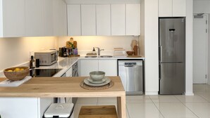 Une cuisine moderne avec des meubles blancs, des appareils en acier inoxydable et une table en bois.
