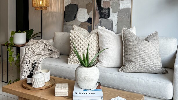 Un salon moderne avec un canapé gris, une table basse en bois et des coussins décoratifs.