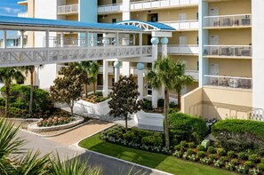 A hotel with multiple floors, a covered walkway, and landscaped gardens with palm trees and flower beds.