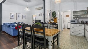 A spacious living area with a blue sofa, wooden dining table, and chairs, a kitchen with white cabinets, and a ceiling with a skylight.